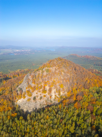 Aerial view of Maly Bezdez hill covered in vibrant autumn foliage surrounded by dense forest and rolling landscape in Bezdez Liberecky kraj Czechia.