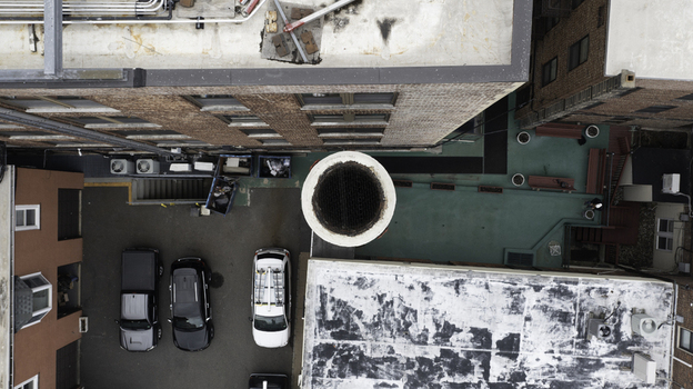 Aerial view of a narrow urban alleyway between brick buildings featuring a large industrial chimney parked vehicles and a green rooftop terrace in Summit New Jersey United States. Aerial view of a narrow urban alleyway between brick buildings featuring a large industrial chimney parked vehicles and a green rooftop terrace in Summit New Jersey United States.