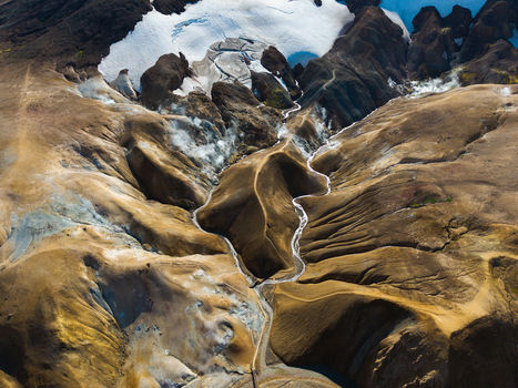 Aerial view of rugged textured mountains meet glacial ice with winding rivers carving through the landscape creating a stunning contrast of earth tones and icy whites Iceland.