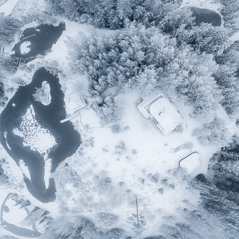 Aerial view of a snow covered landscape featuring a house frozen ponds and frost covered pine trees in Latvia. Aerial view of a snow covered landscape featuring a house frozen ponds and frost covered pine trees in Latvia.