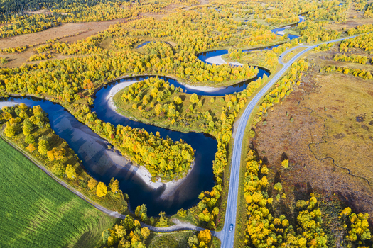 Aerial view of the Ljusnan river winding through a vibrant autumn forest with golden trees and a road running alongside in Bruksvallarna Jamtland County Sweden. Aerial view of the Ljusnan river winding through a vibrant autumn forest with golden trees and a road running alongside in Bruksvallarna Jamtland County Sweden.