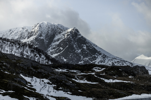 View of snow covered mountain peaks and rocky slopes under a cloudy sky Kvaloya Troms Norway. View of snow covered mountain peaks and rocky slopes under a cloudy sky Kvaloya Troms Norway.
