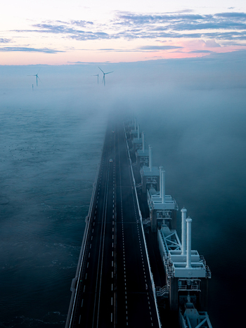 Aerial view of the Delta Projects Netherlands storm surge barrier shrouded in thick morning fog with wind turbines in the distance Vrouwenpolder Zeeland Netherlands.