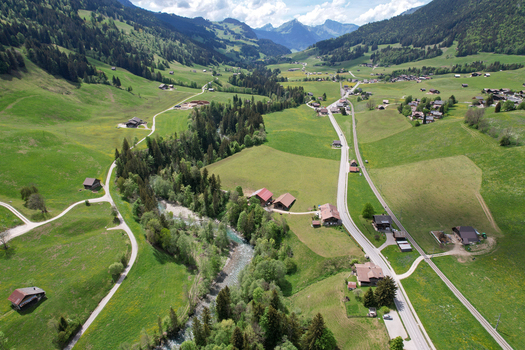 Aerial view of the lush green valley and winding river surrounded by traditional chalets and majestic mountains in Rougemont Vaud Switzerland. Aerial view of the lush green valley and winding river surrounded by traditional chalets and majestic mountains in Rougemont Vaud Switzerland.