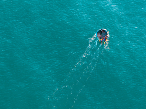Aerial view of a traditional round basket boat with local fishermen navigating the turquoise waters of the sea in Vietnam. Aerial view of a traditional round basket boat with local fishermen navigating the turquoise waters of the sea in Vietnam.
