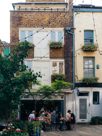 London United Kingdom 20 June 2025 View of diners seated outside a restaurant with the warm brick facade and white window frames contrasting against the lush greenery of hanging planters. London United Kingdom 20 June 2025 View of diners seated outside a restaurant with the warm brick facade and white window frames contrasting against the lush greenery of hanging planters.
