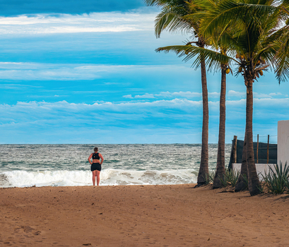 Aerial view of a person standing on the sandy beach of Playa Punta Perula with palm trees and ocean waves under a blue sky in Perula Jalisco Mexico. Aerial view of a person standing on the sandy beach of Playa Punta Perula with palm trees and ocean waves under a blue sky in Perula Jalisco Mexico.