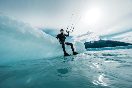 View of a kiteboarder in a wetsuit sitting on a large iceberg in the water with the Perito Moreno glacier in the background Perito Moreno Santa Cruz Province Argentina. View of a kiteboarder in a wetsuit sitting on a large iceberg in the water with the Perito Moreno glacier in the background Perito Moreno Santa Cruz Province Argentina.
