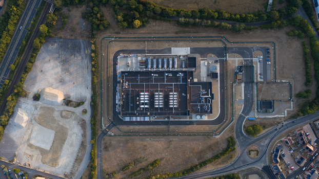Aerial view of a modern data center facility featuring rooftop cooling units and secure perimeter fencing situated near roads and residential areas in Bracknell England United Kingdom.