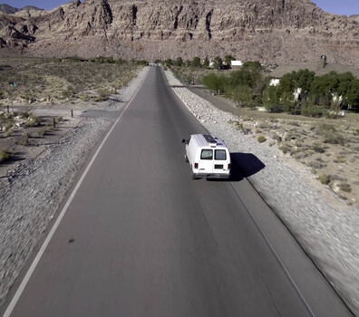 Aerial view of a white van driving down a paved road through the desert landscape of Red Rock NV United States.