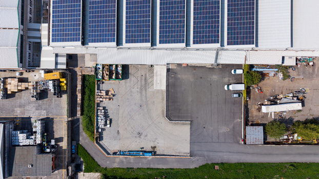 Aerial view of a manufacturing plant featuring large solar panel arrays on the roof a paved loading area with parked delivery vehicles and industrial storage zones in Milan Lombardy Italy. Aerial view of a manufacturing plant featuring large solar panel arrays on the roof a paved loading area with parked delivery vehicles and industrial storage zones in Milan Lombardy Italy.