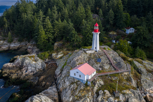 Aerial view of Point Atkinson Lighthouse with its iconic red lantern room set upon rugged coastal rocks and surrounded by dense evergreen forest in West Vancouver British Columbia Canada.