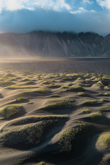 Aerial view of the dramatic black sand dunes and grassy mounds at the base of Vestrahorn mountain under a cloudy sky in Sveitarfelagid Hornafjordur Iceland. Aerial view of the dramatic black sand dunes and grassy mounds at the base of Vestrahorn mountain under a cloudy sky in Sveitarfelagid Hornafjordur Iceland.