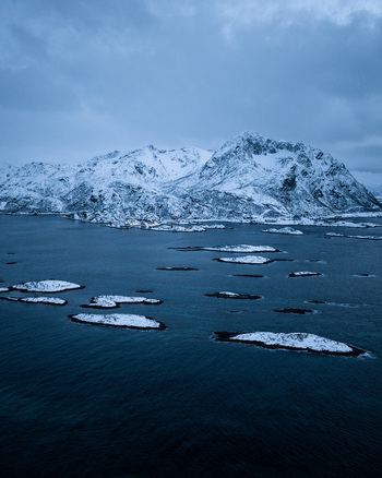Aerial view of snow dusted islands scattered across the dark cold waters contrasting against the stark white mountain backdrop Hamn Troms Norway. Aerial view of snow dusted islands scattered across the dark cold waters contrasting against the stark white mountain backdrop Hamn Troms Norway.