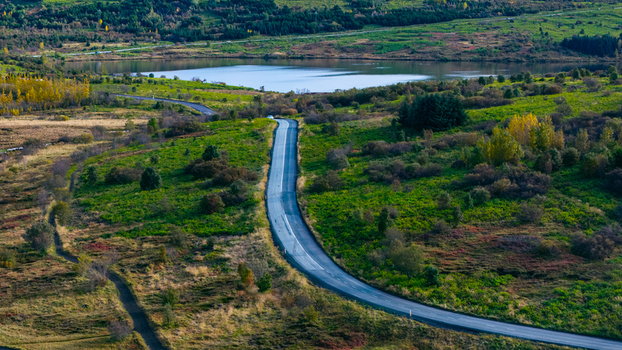 Aerial view of a winding road cutting through a vibrant landscape with autumn colors lush green vegetation and a serene lake in Iceland. Aerial view of a winding road cutting through a vibrant landscape with autumn colors lush green vegetation and a serene lake in Iceland.