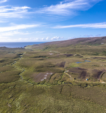 Aerial view of the rugged moorland and peat bogs of An Port with a winding stream and rolling hills under a bright blue sky in Ardara County Donegal Ireland.