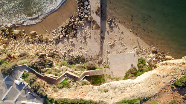 Aerial view of the coastline at Ferragudo featuring a zigzagging staircase leading down to a sandy beach rocky cliffs and a concrete pier in Ferragudo Faro District Portugal.