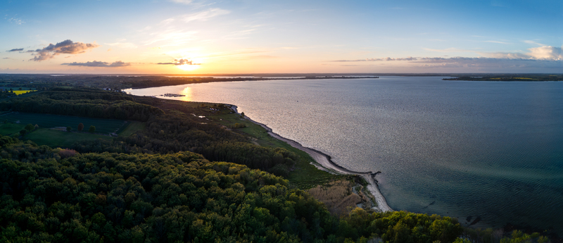 Aerial view of Bockholmwik coastline with lush green forests and calm waters under a golden sunset sky in Munkbrarup Schleswig Holstein Germany. Aerial view of Bockholmwik coastline with lush green forests and calm waters under a golden sunset sky in Munkbrarup Schleswig Holstein Germany.