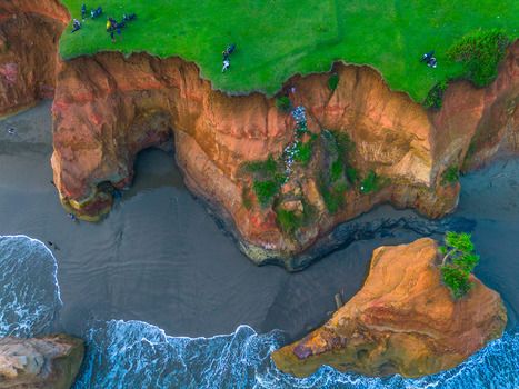Aerial view of the dramatic red coastal cliffs with lush green grass black sand beach and crashing ocean waves in Bali Indonesia. Aerial view of the dramatic red coastal cliffs with lush green grass black sand beach and crashing ocean waves in Bali Indonesia.