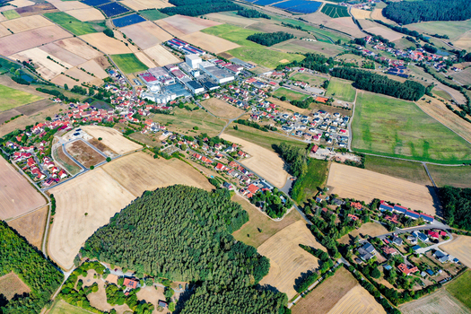 Aerial view of the town of Vestenbergsgreuth featuring residential houses industrial buildings and vast agricultural fields in Bavaria Germany.