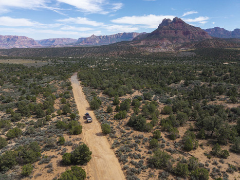 Aerial view of a SUV pulling a teardrop camper trailer along a dirt road on Gooseberry Mesa with Zion National Park in the background in Hurricane Utah United States. Aerial view of a SUV pulling a teardrop camper trailer along a dirt road on Gooseberry Mesa with Zion National Park in the background in Hurricane Utah United States.