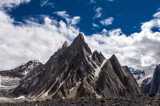 View of the dramatic rocky peaks and snow covered slopes of the Baltoro Glacier under a bright blue sky with scattered clouds in the Karakoram range Baltoro Gilgit Baltistan Pakistan.