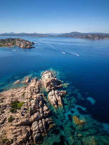 Aerial view of the granite rock formations of Carlotto along the turquoise coastline with boats sailing in the distance in La Maddalena Sardinia Italy. Aerial view of the granite rock formations of Carlotto along the turquoise coastline with boats sailing in the distance in La Maddalena Sardinia Italy.