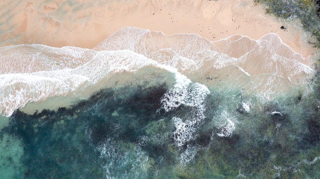 Aerial view of turquoise waves crashing on the sandy shore of Constantine Bay with rocky outcrops in Padstow Cornwall United Kingdom. Aerial view of turquoise waves crashing on the sandy shore of Constantine Bay with rocky outcrops in Padstow Cornwall United Kingdom.