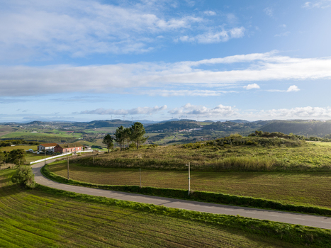 Aerial view of rolling green hills a winding asphalt road and distant wind turbines under a blue sky with soft clouds in Portugal. Aerial view of rolling green hills a winding asphalt road and distant wind turbines under a blue sky with soft clouds in Portugal.
