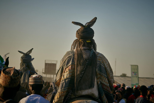 Zaria City Nigeria 22 March 2026 View of a prominent figure in elaborate traditional attire with distinctive horned headwear amidst a bustling crowd under a soft clear sky. Zaria City Nigeria 22 March 2026 View of a prominent figure in elaborate traditional attire with distinctive horned headwear amidst a bustling crowd under a soft clear sky.