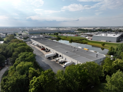 Aerial view of an industrial warehouse facility featuring loading docks with parked semi trucks a large solar panel array and a retention pond in Indianapolis Indiana United States. Aerial view of an industrial warehouse facility featuring loading docks with parked semi trucks a large solar panel array and a retention pond in Indianapolis Indiana United States.