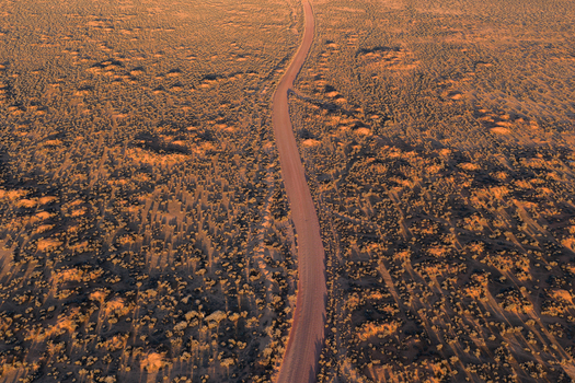 Aerial view of a winding dirt road cutting through the vast arid outback landscape with low scrub and long shadows during golden hour in Flinders Ranges South Australia Australia. Aerial view of a winding dirt road cutting through the vast arid outback landscape with low scrub and long shadows during golden hour in Flinders Ranges South Australia Australia.