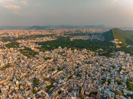 Aerial view of the dense urban landscape of Udaipur featuring traditional rooftops a large green park and surrounding hills under the golden hour light in Udaipur Rajasthan India. Aerial view of the dense urban landscape of Udaipur featuring traditional rooftops a large green park and surrounding hills under the golden hour light in Udaipur Rajasthan India.