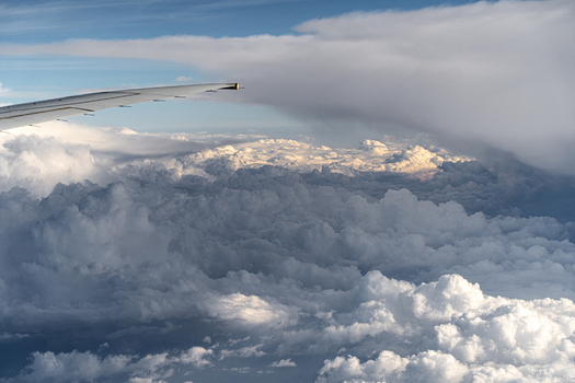 Aerial view of an airplane wing flying above a dense layer of white fluffy clouds under a blue sky India. Aerial view of an airplane wing flying above a dense layer of white fluffy clouds under a blue sky India.