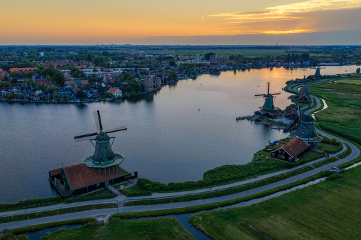 Aerial view of Zaanse Schans Windmill with traditional wooden houses along the riverbank at sunset in Zaandam Noord Holland Netherlands.
