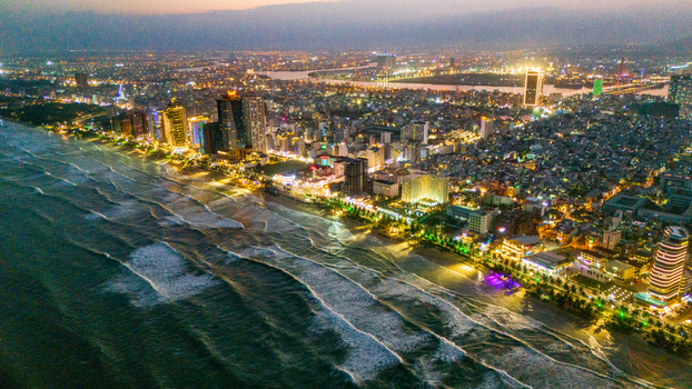 Aerial view of the illuminated coastline of Da Nang at night featuring high rise hotels vibrant city lights and waves crashing onto the sandy beach in Da Nang Vietnam. Aerial view of the illuminated coastline of Da Nang at night featuring high rise hotels vibrant city lights and waves crashing onto the sandy beach in Da Nang Vietnam.
