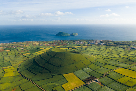 Aerial view of Pico Dona Joana volcanic cone surrounded by green patchwork fields and stone walls overlooking the Atlantic Ocean Feteira Acores Portugal.
