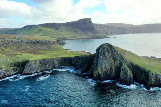 Aerial view of Neist Point Lighthouse perched on dramatic sea cliffs with rugged green hills and the Atlantic Ocean on the Isle of Skye Scotland United Kingdom.