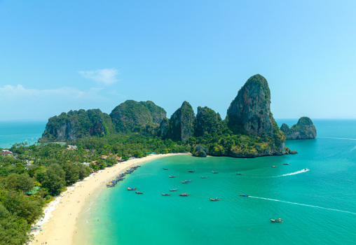 Aerial view of Railay Beach with its iconic limestone cliffs turquoise waters and traditional long tail boats anchored along the sandy shore in Ao Nang Krabi Thailand.