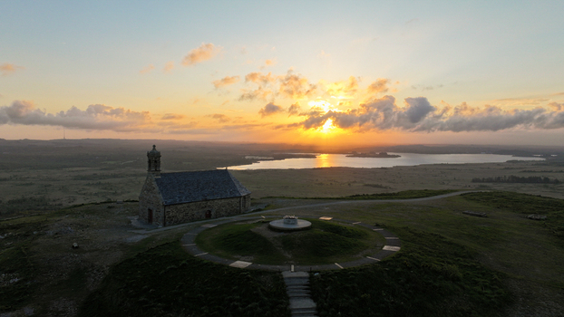 Aerial view of Chapelle Saint Michel de Brasparts on a hilltop overlooking a lake during a golden sunset in Saint Rivoal Bretagne France. Aerial view of Chapelle Saint Michel de Brasparts on a hilltop overlooking a lake during a golden sunset in Saint Rivoal Bretagne France.