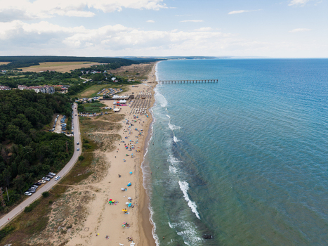 Aerial view of the sandy beach at Shkorpilovtsi with a long pier extending into the Black Sea bordered by lush green forests and a coastal road in Shkorpilovtsi Varna Bulgaria. Aerial view of the sandy beach at Shkorpilovtsi with a long pier extending into the Black Sea bordered by lush green forests and a coastal road in Shkorpilovtsi Varna Bulgaria.