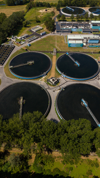 Aerial view of a wastewater treatment plant featuring large circular sedimentation tanks surrounded by lush green trees and industrial infrastructure in Milan Lombardy Italy. Aerial view of a wastewater treatment plant featuring large circular sedimentation tanks surrounded by lush green trees and industrial infrastructure in Milan Lombardy Italy.