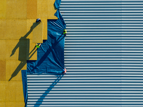 Aerial view of workers in high visibility vests installing yellow insulation panels and blue protective sheeting on a corrugated metal roof in Belgrade City of Belgrade Serbia. Aerial view of workers in high visibility vests installing yellow insulation panels and blue protective sheeting on a corrugated metal roof in Belgrade City of Belgrade Serbia.