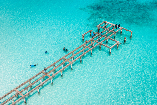 Aerial view of a wooden jetty extending into clear turquoise water with people swimming and walking on the structure in Vashafaru Haa Alif Atoll Maldives. Aerial view of a wooden jetty extending into clear turquoise water with people swimming and walking on the structure in Vashafaru Haa Alif Atoll Maldives.