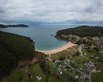 Aerial view of Xilloi Beach featuring golden sand and turquoise waters surrounded by dense green forests and a small village in Vicedo Lugo Spain. Aerial view of Xilloi Beach featuring golden sand and turquoise waters surrounded by dense green forests and a small village in Vicedo Lugo Spain.