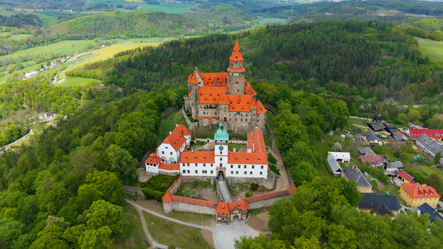 Aerial view of Bouzov Castle with its iconic red tiled roofs and tall tower surrounded by lush green forests and rolling hills in Bouzov Olomoucky kraj Czechia. Aerial view of Bouzov Castle with its iconic red tiled roofs and tall tower surrounded by lush green forests and rolling hills in Bouzov Olomoucky kraj Czechia.