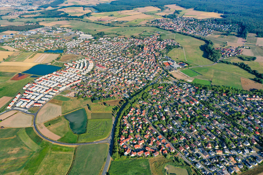 Aerial view of the town of Adelsdorf featuring residential houses with red roofs surrounding green agricultural fields and dense forests in Adelsdorf Bavaria Germany.