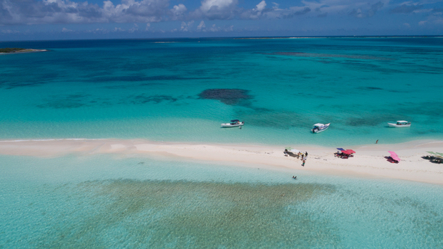 Aerial view of Los Roques archipelago featuring a white sandbar in turquoise water with boats anchored nearby and people on the beach in Los Roques Dependencias Federales Venezuela. Aerial view of Los Roques archipelago featuring a white sandbar in turquoise water with boats anchored nearby and people on the beach in Los Roques Dependencias Federales Venezuela.