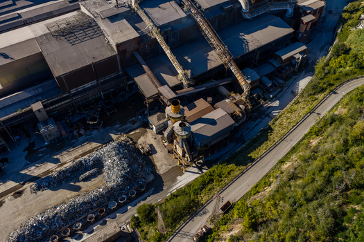 Aerial view of the Acciai Speciali Terni steel plant featuring large industrial buildings metal scrap piles conveyor systems and chimneys in Terni Umbria Italy.