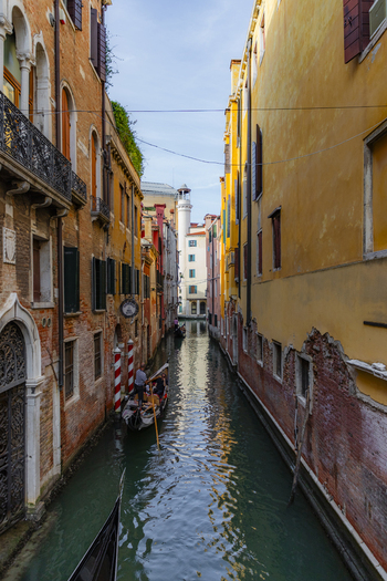 Venice Italy 21 September 2026 View of a narrow canal in Venice with a gondolier navigating a gondola past historic yellow and orange buildings under a clear blue sky. Venice Italy 21 September 2026 View of a narrow canal in Venice with a gondolier navigating a gondola past historic yellow and orange buildings under a clear blue sky.